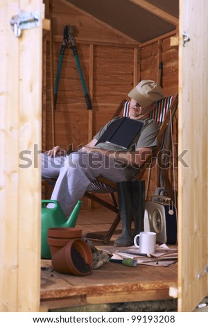 Man sitting in deckchair falling asleep in the shed while reading book