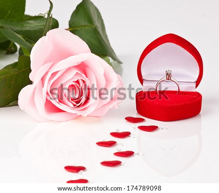 A pink rose with a diamond engagement ring in velvet box. Image is isolated on white.