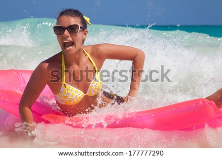 Young smiling woman having fun on pink air bed in sea water. Beautiful Woman Relaxing in turquoise Water. Hot Girl enjoying the Waves of the Ocean
