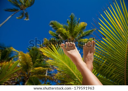 Beauty woman slim legs with fashion nails on palm trees background. Summer holidays.