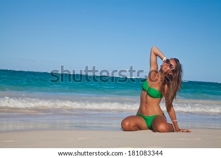 Happy blissful young woman in green bikini in meditation enjoying summer sun and tanning during holidays on Hawaii. Smiling beautiful woman sunbathing on the Hawaiian beach. Travel concept.