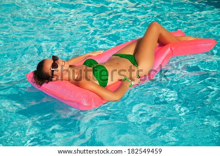 Sexy smiling girl in beautiful bikini relax on pink air bed in swimming pool. Beautiful Woman Relaxing in turquoise water, at luxury travel resort.