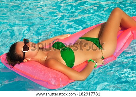 Sexy girl in green bikini relax on pink air bed in swimming pool. Beautiful Woman Relaxing at luxury travel resort.