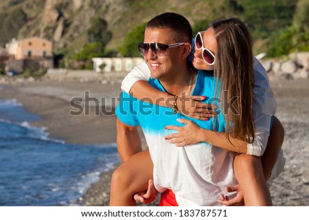 Love - Happy couple on beach having fun piggyback. Smiling happy couple laughing together on romantic holidays vacation travel trip in Sicily.