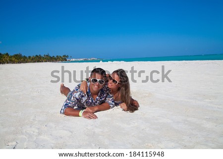 Happy young couple lying on sand under sunny summer sun. Summer holidays vacation on tropical beach.