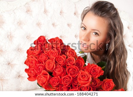 Portrait of attractive brunette smiling woman with a large bouquet of red roses in her arms. Holidays and celebrations concepts.