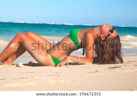 Happy blissful young woman in green bikini enjoying summer sun and tanning during holidays on Hawaii. Smiling beautiful woman sunbathing on the Hawaiian beach. Travel concept.