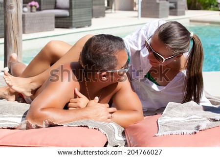 Sexy and attractive couple lying on luxury sun bed on a tropical garden, near a swimming pool.