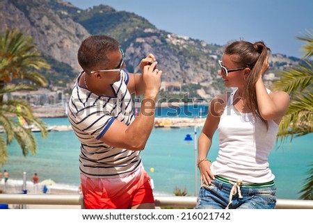Fun couple travel. Man taking photo picture of women smiling happy. Couple on summer holidays vacation on tropical beach.