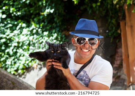 Man in summer hat holding black cat smiling happy.