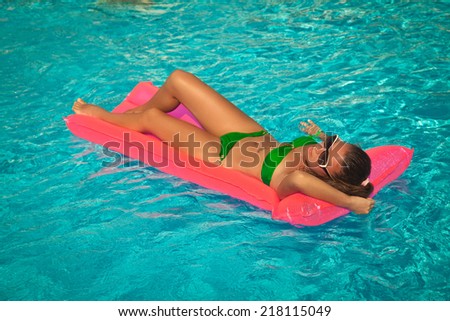 Sexy girl in green bikini floating on pink air bed in swimming pool. Beautiful Woman Relaxing at luxury travel resort.