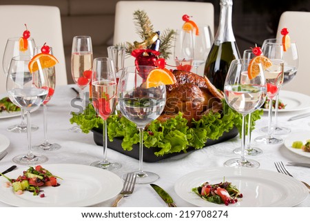 Garnished roast turkey on Christmas-decorated table, beautiful glasses champagne and food