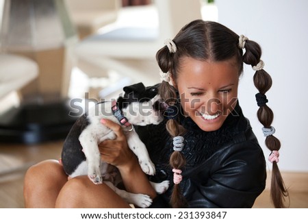 Portrait of young woman playing with baby dog, puppy bites in womans hair (focus on face)
