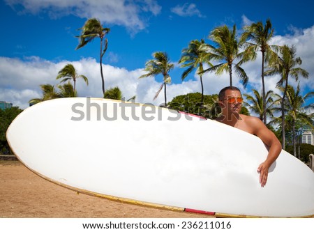 Attractive masculine young man holding his surfboard on the tropical beach. Photo from Waikiki beach, Honolulu, Hawaii.