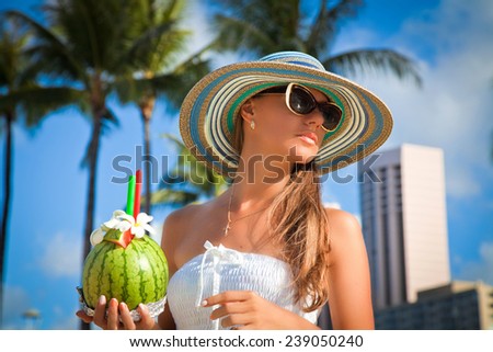 Glamorous woman in beautiful summer hat enjoying the perfect summer day with exotic cocktail on tropical resort. Summer luxury vacation in Hawaii.