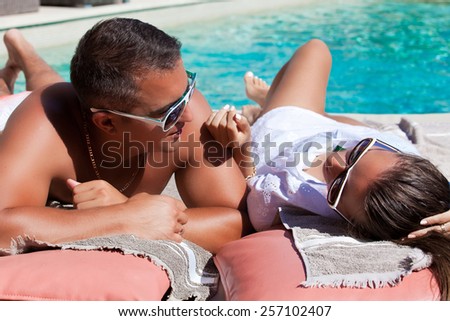 Shot of young couple relaxing at the luxury poolside, at travel spa resort pool. Couple in love, summer luxury vacation in Europe. Travel holidays concept.