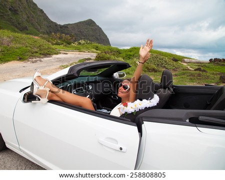 Happy beautiful young woman sitting in a sports car on beautiful summer day. Sexy woman\'s legs showing out of the car, enjoying freedom feeling happy on the Hawaii.