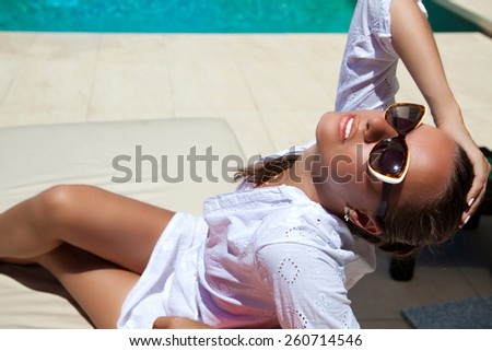 Sexy beautiful woman holding hand behind head, relaxing at the luxury poolside. Girl at travel spa resort pool. Summer luxury vacation. (focus on woman face)