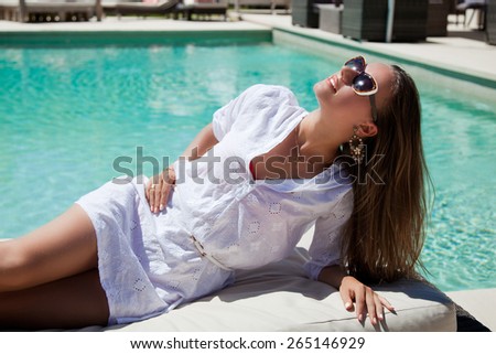 Beautiful woman relaxing enjoying sun at the luxury poolside, tanning. Girl at travel spa resort pool. Summer luxury vacation.