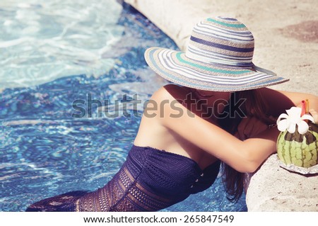 Pretty young woman in sexy bikini at edge of a swimming pool with exotic cocktail. Girl at travel spa resort pool. Summer luxury vacation.