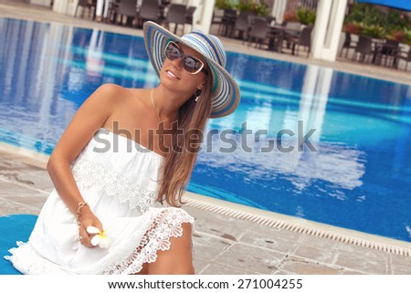 Sexy cheerful woman in summer white dress, relaxing at the luxury poolside. Girl at travel spa resort pool. Summer luxury vacation.