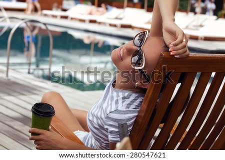 Shot of a young woman with morning coffee relaxing outdoors while on vacation. Beautiful woman, relaxing beside a luxury swimming pool. Girl at travel spa resort pool. (focus on woman face)