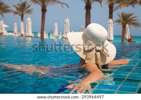 Woman in big straw hat relaxing  in a exotic swimming pool. Girl at travel spa resort pool. Summer luxury vacation.
