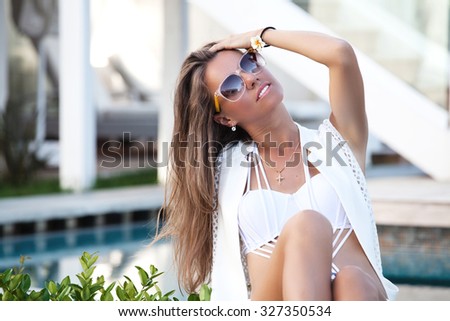 Attractive woman relaxing on luxurious villa. Sitting near swimming pool. Luxury spa resort, travel and tourism concept.