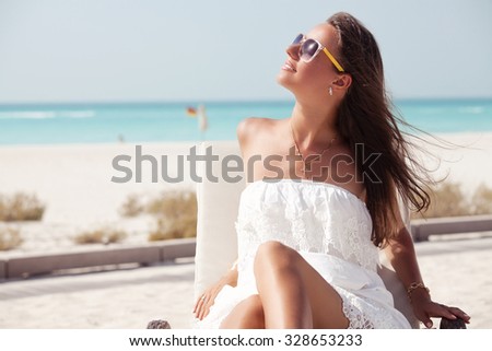 Beach woman in white dress enjoying the summer sun happy sitting in a sunbed at the tropica beach with face raised to the sunlight.