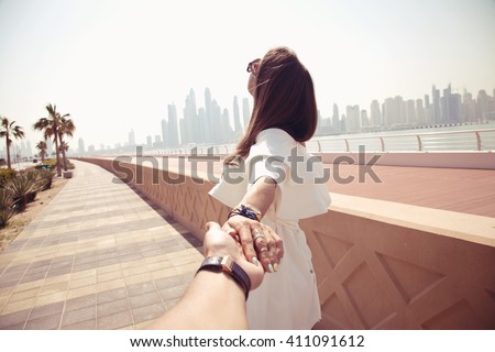 Couple summer vacation travel. Woman walking on romantic honeymoon promenade holidays holding hand of husband following her, view from behind. (focus on woman)