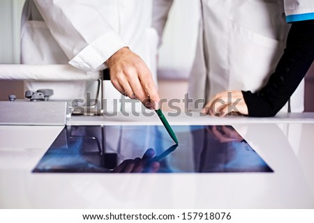 Medicine lab doctor pointing on x-ray that is lying on a table with a nurse no face