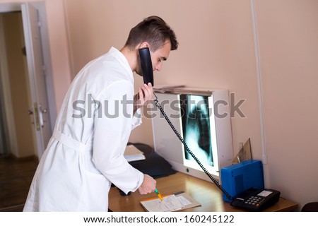 A male doctor in a white coat making a call with a check-list in a clinic medical lab