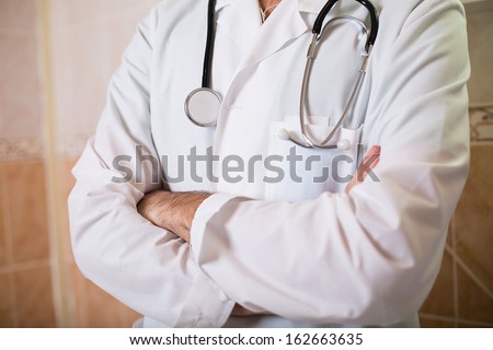 A chest of a male doctor in a clinic with a stethoscope no face hands crossed