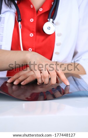 Young woman doctor in red uniform and white medical gown with a stethoscope hanging on chest, hands lying on x-ray photograph with no face