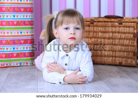 A three year old girl lying on the floor in a pink room, in white blouse with makeup red lips