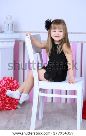 A three year old child girl in a black cocktail dress with a hairstyle and makeup. red lips, happy smiling