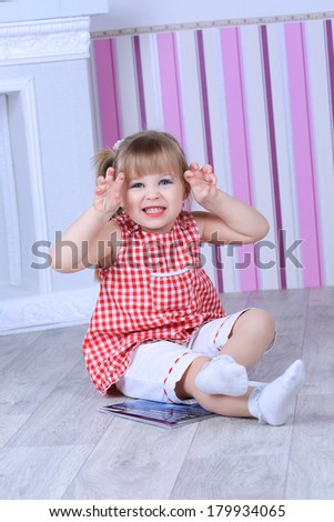 A three year old girl posing like a model in a pink room, in white blouse and pink pants with makeup red lips and a hairstyle making funny face expression