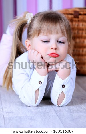 A three year old girl lying on the floor in a pink room, in white blouse with makeup red lips sad face expression