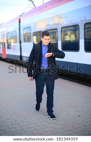 A businessman standing in front of a train checking the time on watch