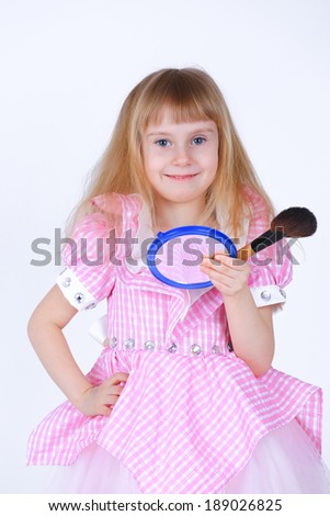 Little girl with a makeup brush and a small mirror in studio