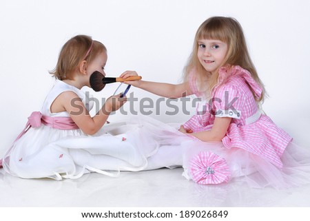 Two little girls with a makeup brush and a small mirror in studio