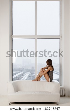 Young beautiful woman sitting on a white couch near the window