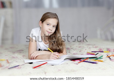 Young cute girl lying on bed and drawing with color pencils