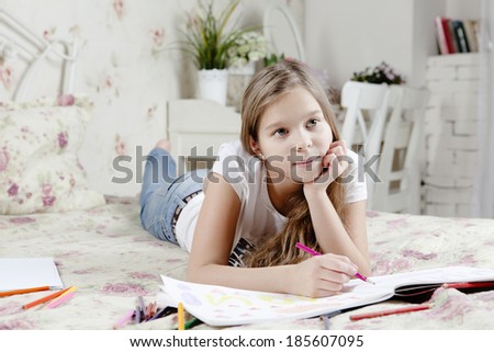 Young cute girl lying on bed and drawing with color pencils