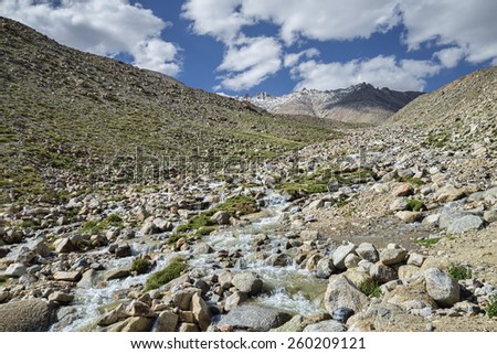 Mountain river flowing among snow summits and green valley