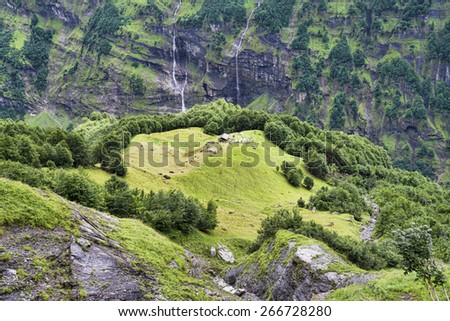 Alpine house on green meadow summer landscape among rock walls and waterfalls