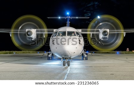 White commercial plane with engines running and propeller blur on a night with the moon on background