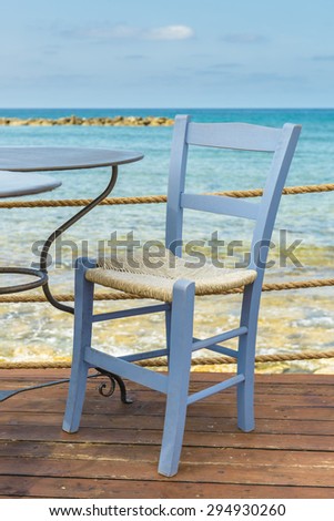 Wooden chair on outdoor deck cafe overlooking the clear blue Mediterranean Sea in Paphos, Cyprus.