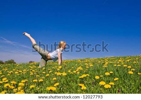 young female exercising yoga on flowery meadow