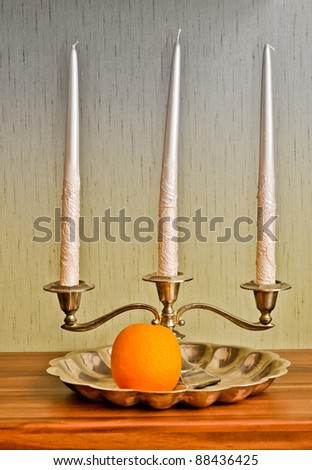 Three candles, silver plate and ripe orange. Still life in HDR technique